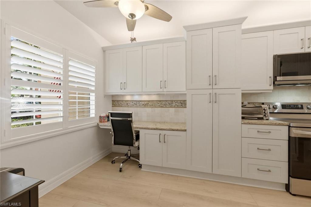 White kitchen with plantation shutters, granite counters, stainless appliances, and a built-in desk nook.