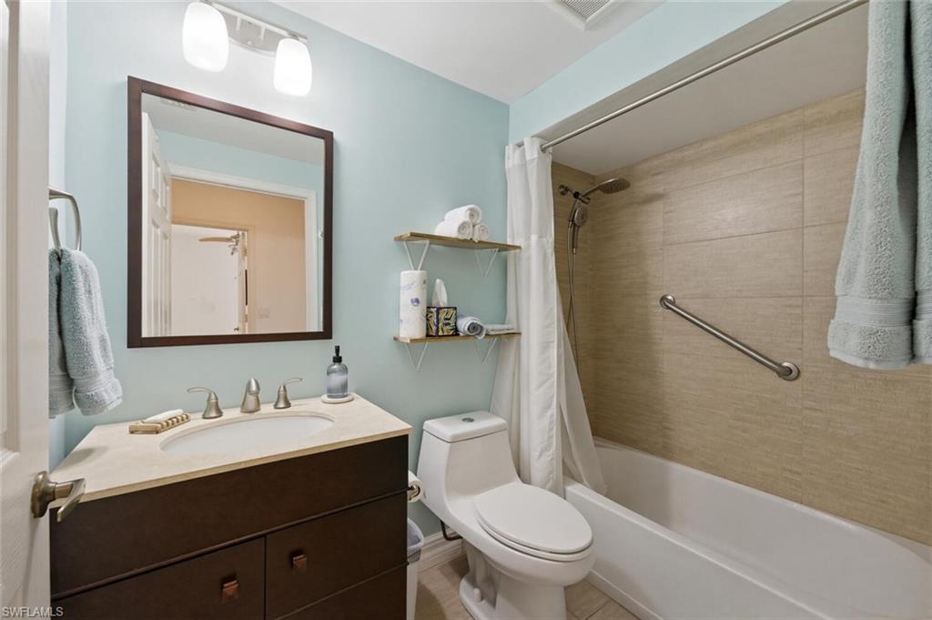Bathroom with dark wood vanity and white tub surrounded by beige tile.