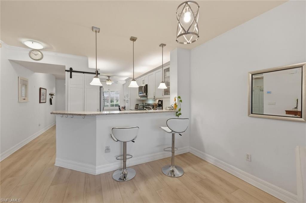 Open kitchen with white cabinets, a breakfast peninsula, two bar stools, and light wood flooring.