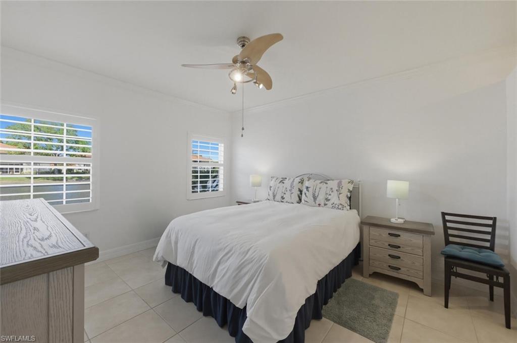 Bedroom with a large bed, floral headboard, ceiling fan, and two shuttered windows.