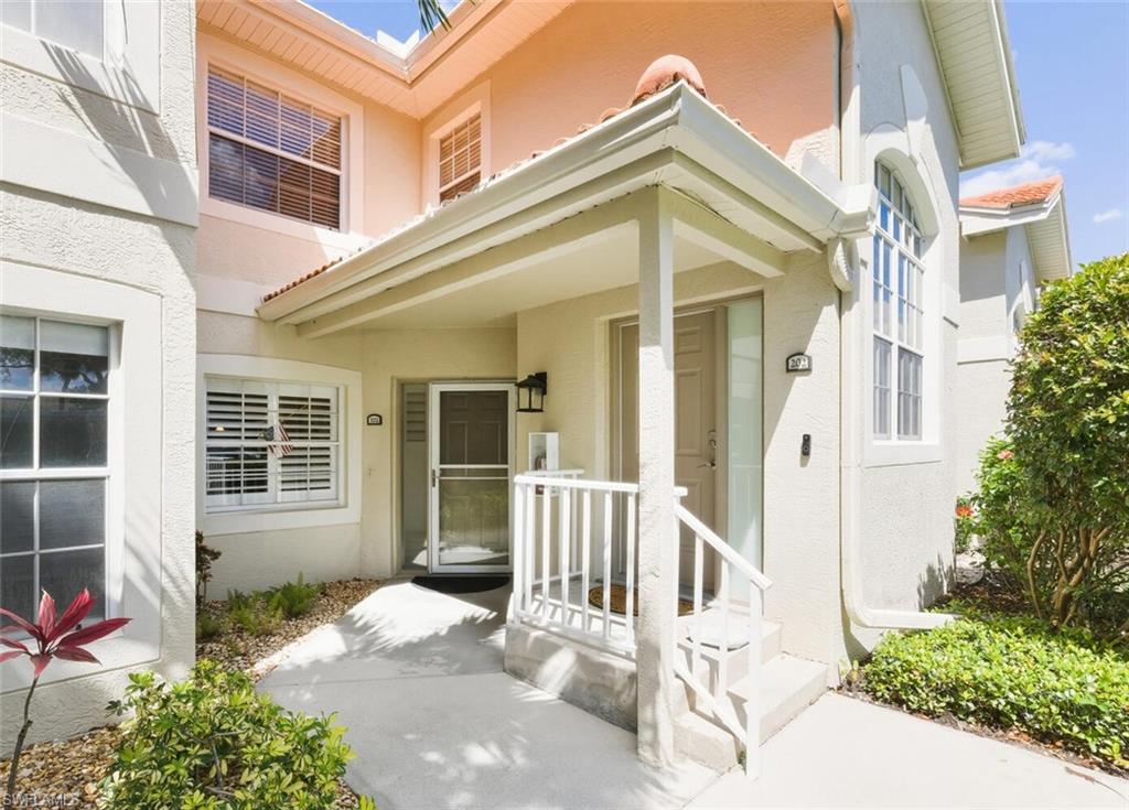 Stucco home entrance with a covered porch, white railings, and landscaped shrubs.