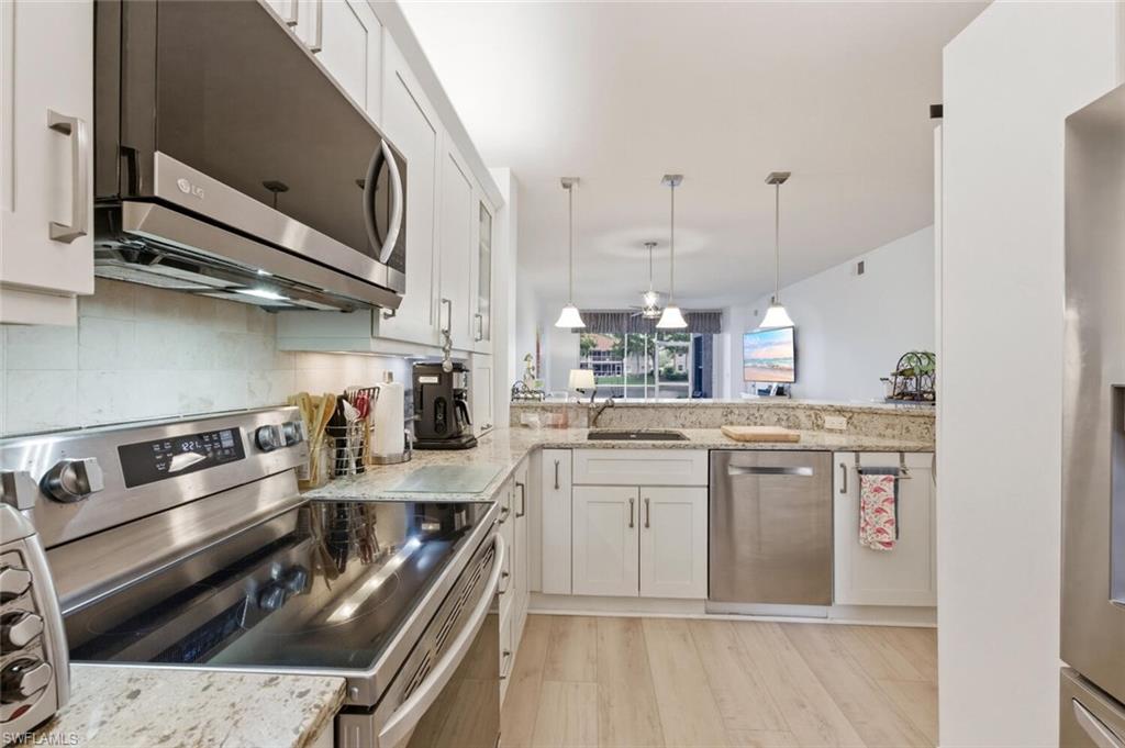 Kitchen with white cabinets, granite counters, stainless steel appliances, and a view toward the living area.