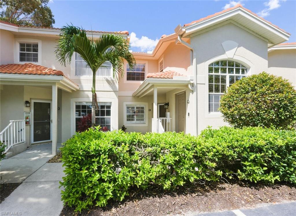 Two-story stucco residence with a terracotta tile roof, arched window, palm tree, and trimmed hedges.