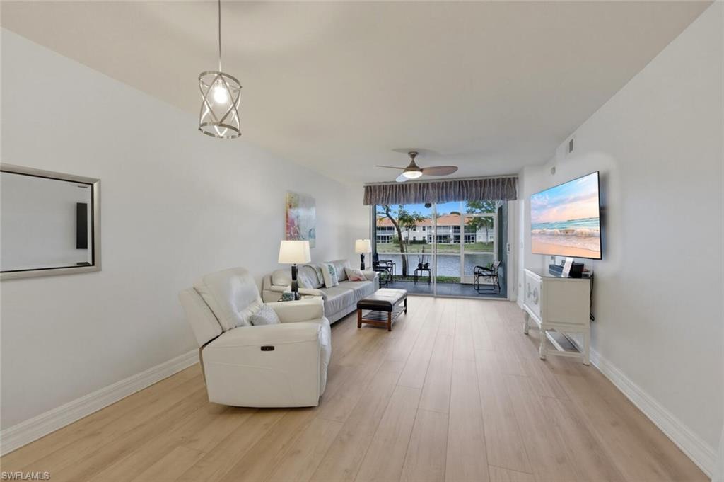 Living room with white sofas and pale wood floors, looking through glass doors onto the water.