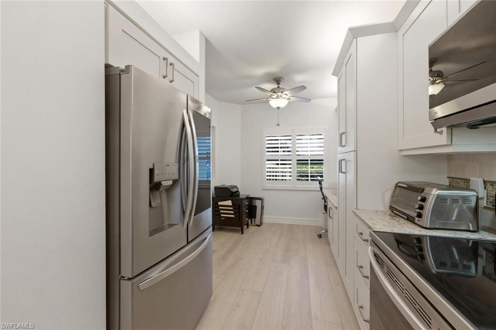 Bright galley kitchen with white cabinets, stainless steel appliances, and a shuttered window.