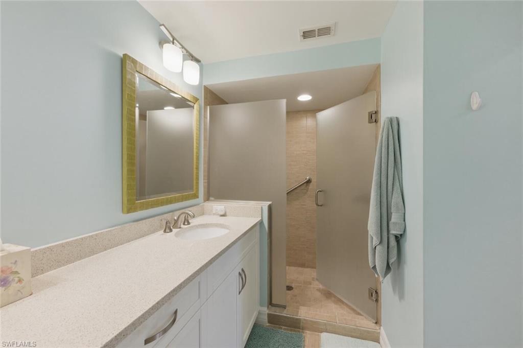 Bathroom with a long white vanity, gold-framed mirror, and open tiled shower.