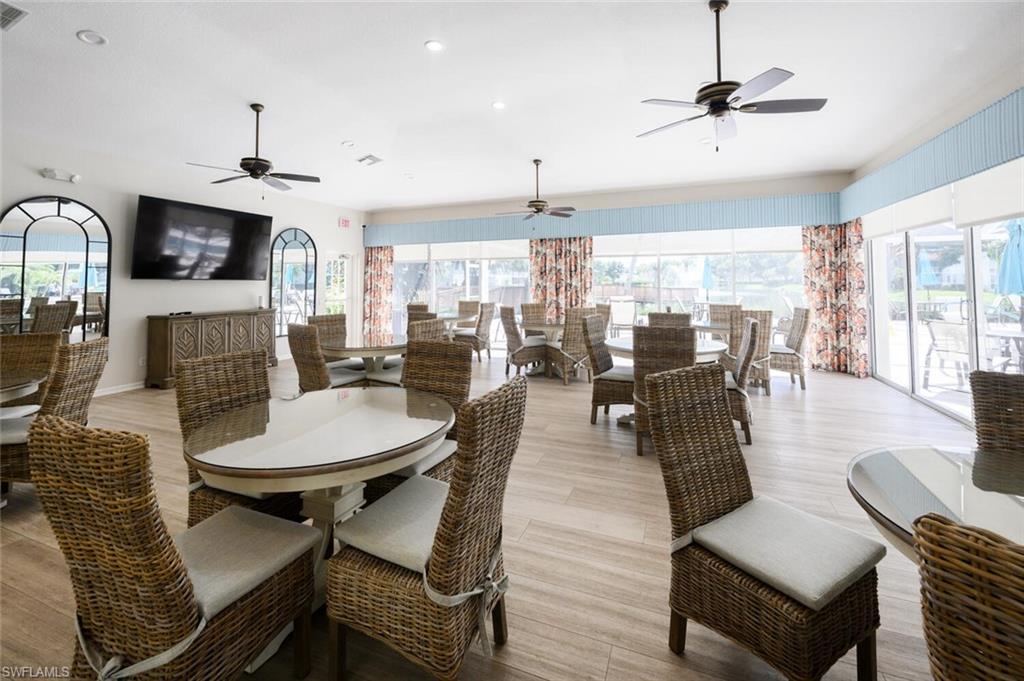 Furnished community dining room with wicker seating, ceiling fans, and walls of windows.