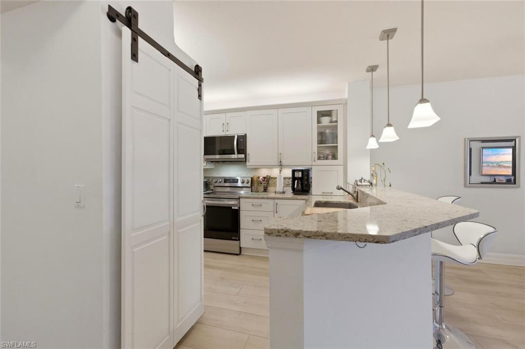 Kitchen with white cabinets, stainless steel appliances, and a granite peninsula beneath pendant lights.