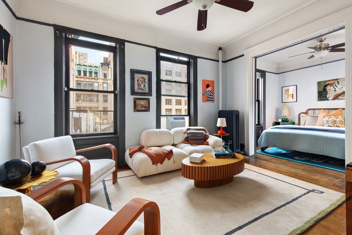 Furnished living room with large city-view windows and an adjoining bedroom.