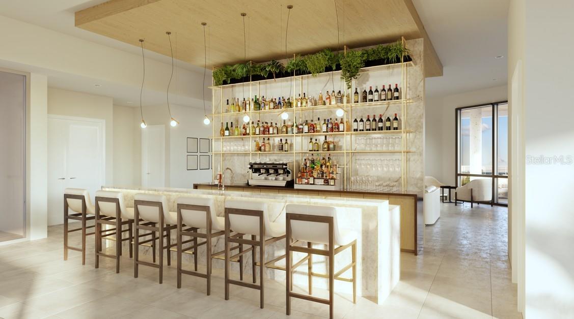 Modern bar with a pale stone counter, upholstered stools, and bottle-lined shelves topped with greenery.