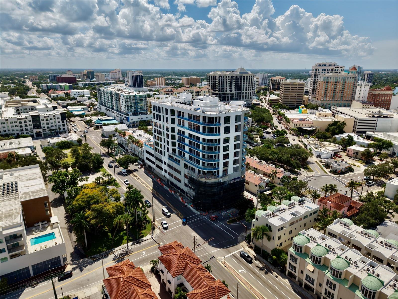 Aerial view of downtown buildings, with a white high-rise featuring curved blue-glass balconies in the foreground.