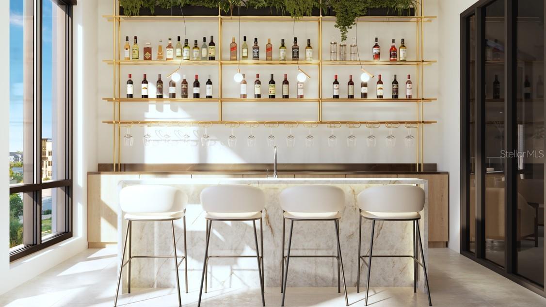 Interior bar with a marble-fronted counter, four white stools, and brass shelves of bottles.