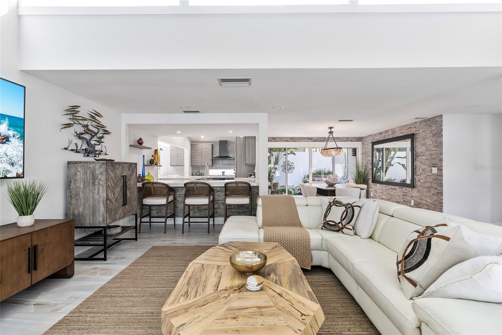 Open-plan living room with white sectional, wood coffee table, stone accent wall, and kitchen island.