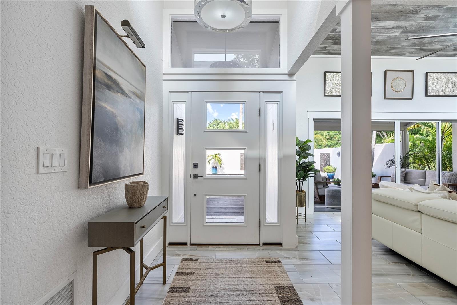 Furnished foyer with a modern white front door, tiled floor, and view into the bright living room.