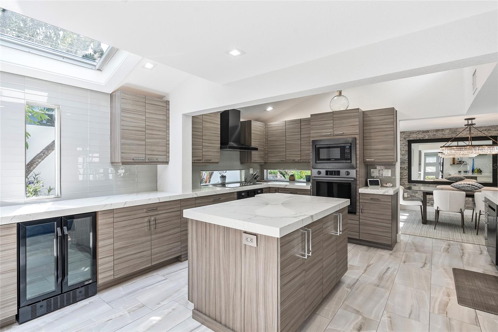 Modern kitchen with a large veined-stone island, gray cabinetry, and a skylight.