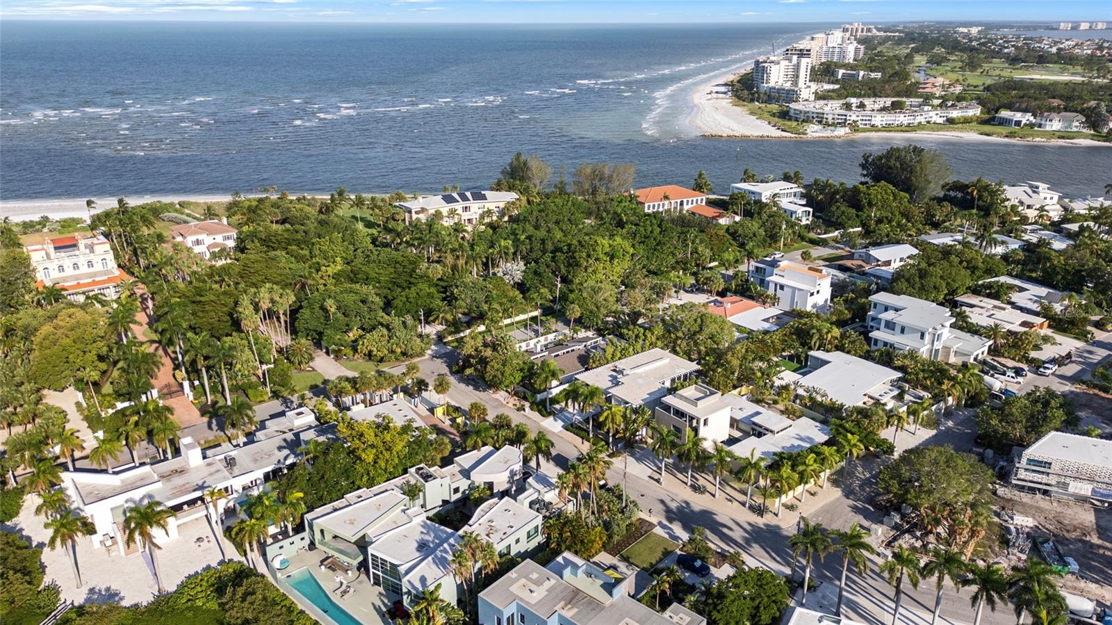 Aerial view of coastal homes and palm trees beside a sandy beach and ocean.