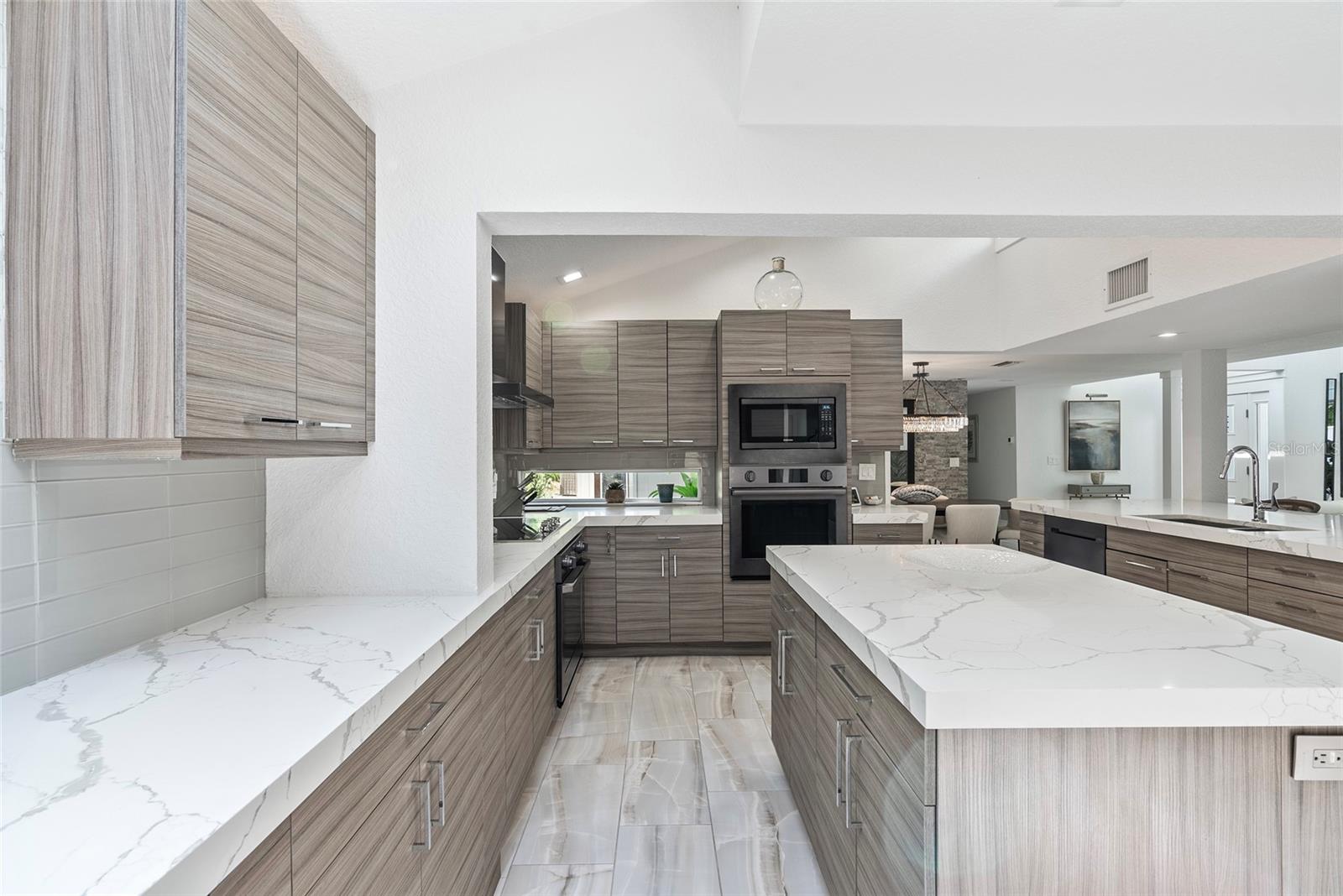 Modern kitchen with gray wood-grain cabinets, veined stone counters, a large island, and built-in appliances.
