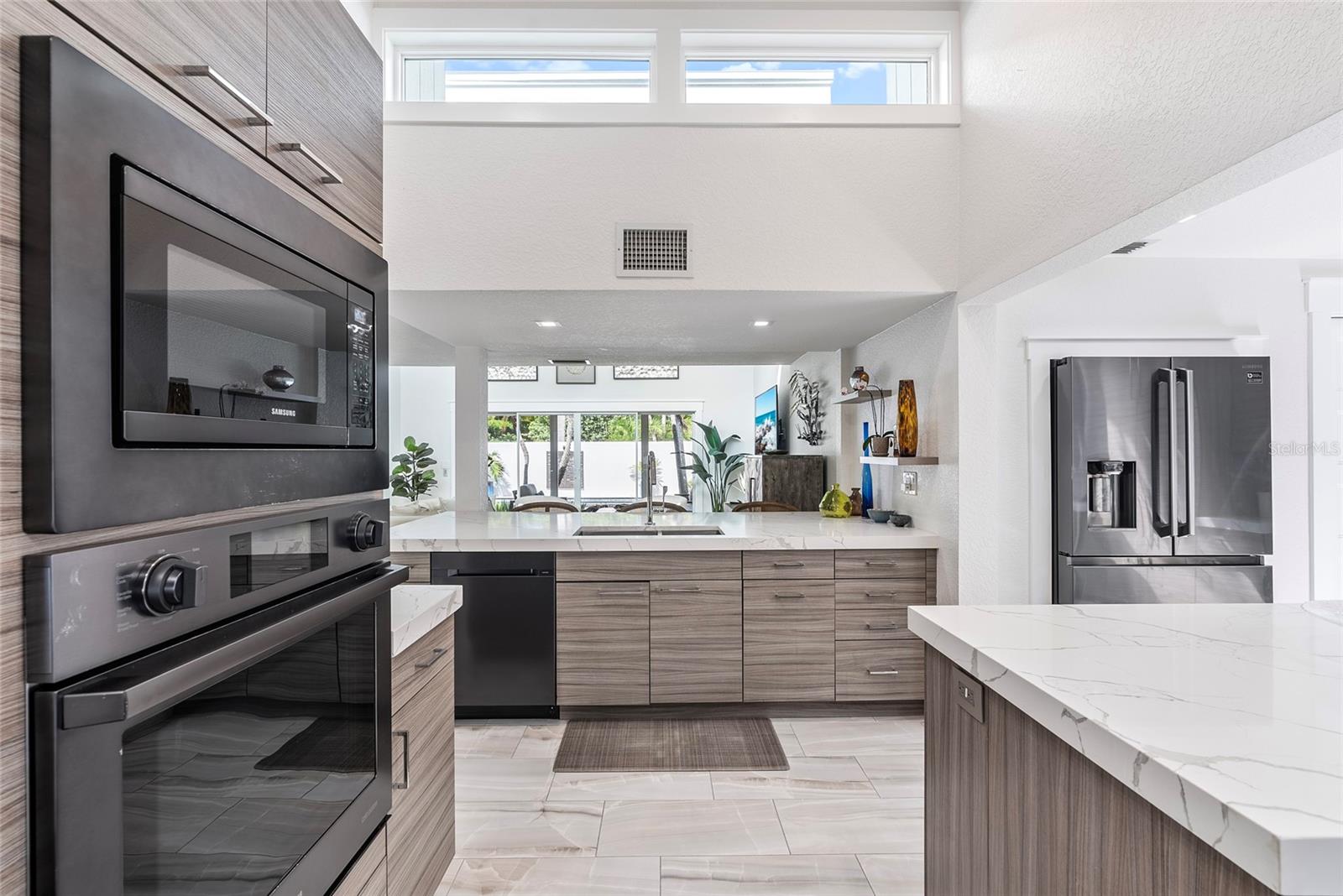 Modern kitchen with gray cabinetry, veined stone counters, and stainless steel appliances opening toward sliding glass doors.