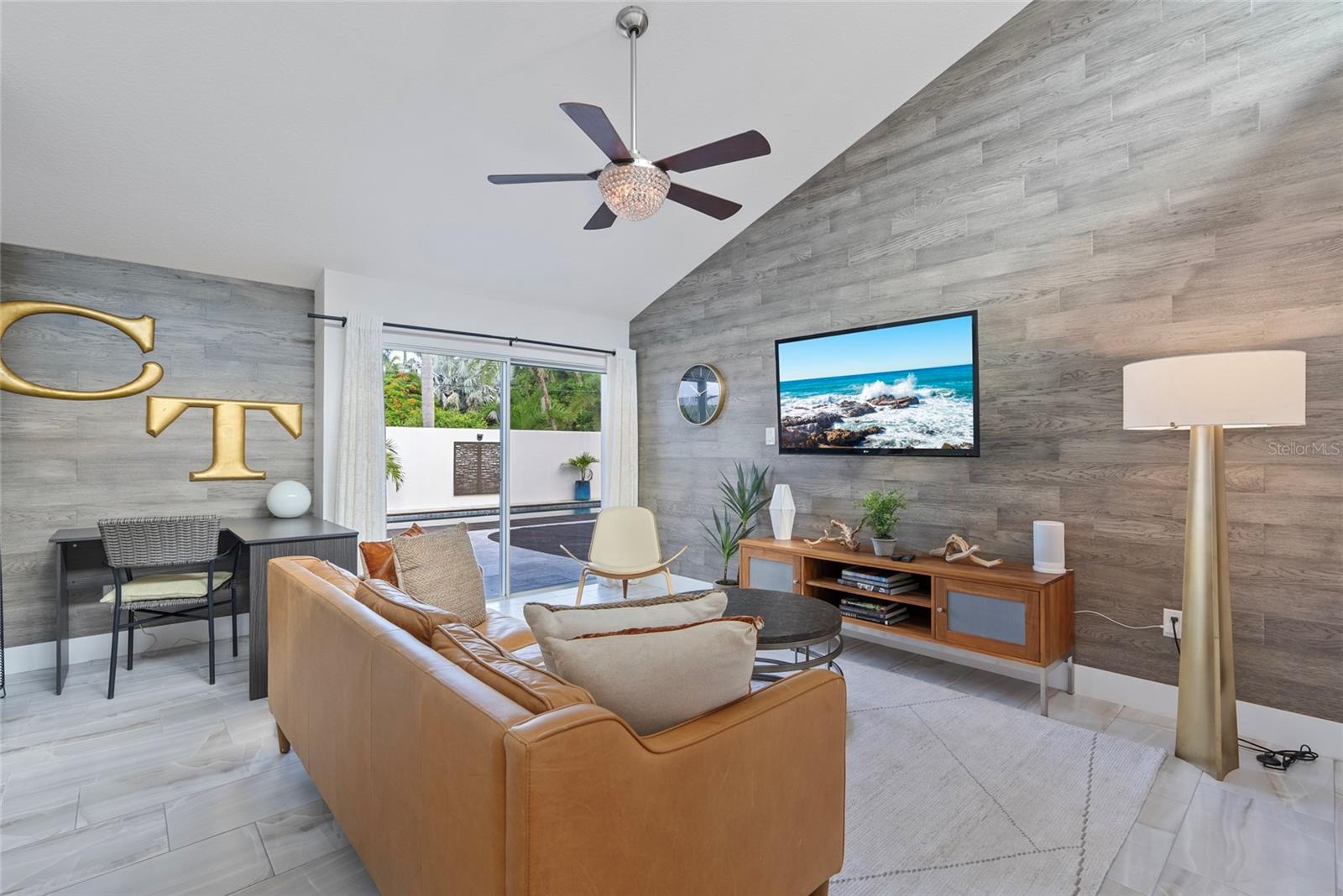 Living room with a tan leather sectional, gray wood accent walls, and sliding doors to a pool patio.