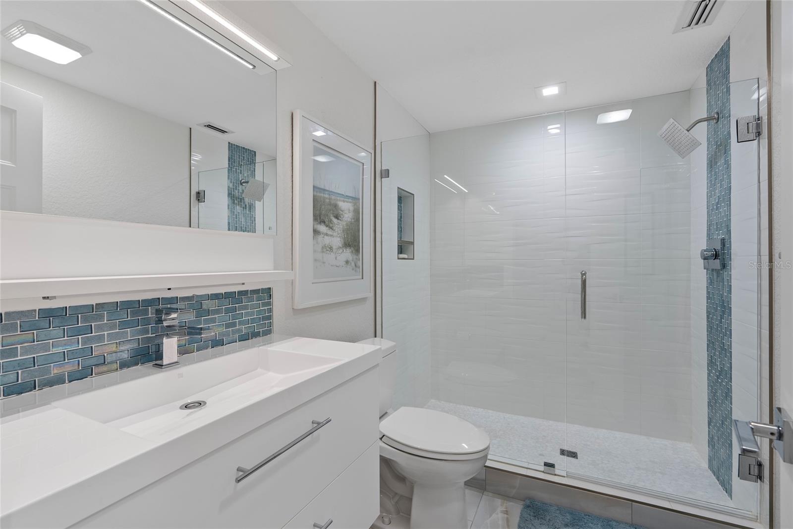 Modern bathroom with a white vanity, blue mosaic backsplash, and glass-enclosed shower.