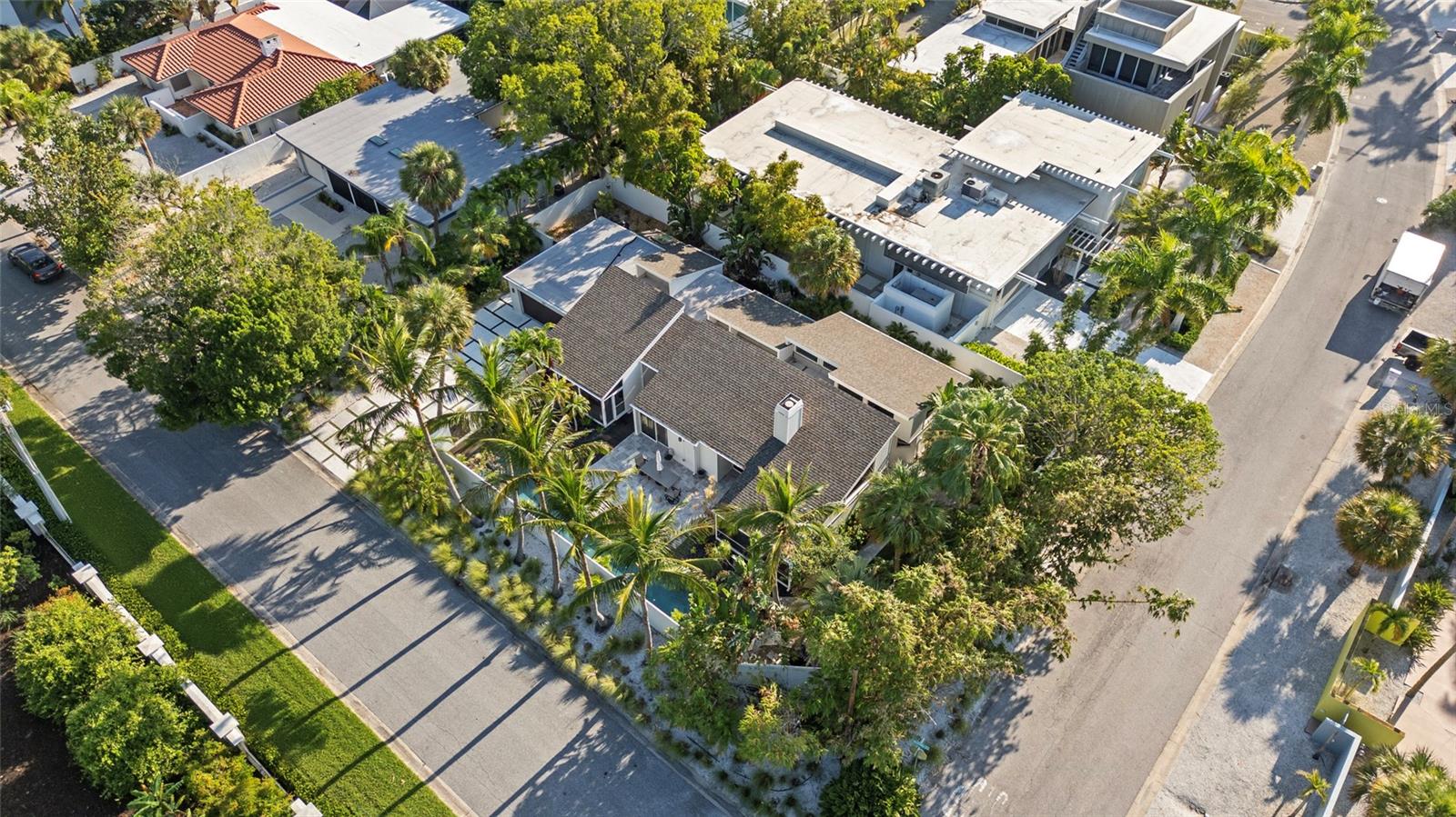 Aerial view of a tan-roofed home among palm trees and neighboring houses.