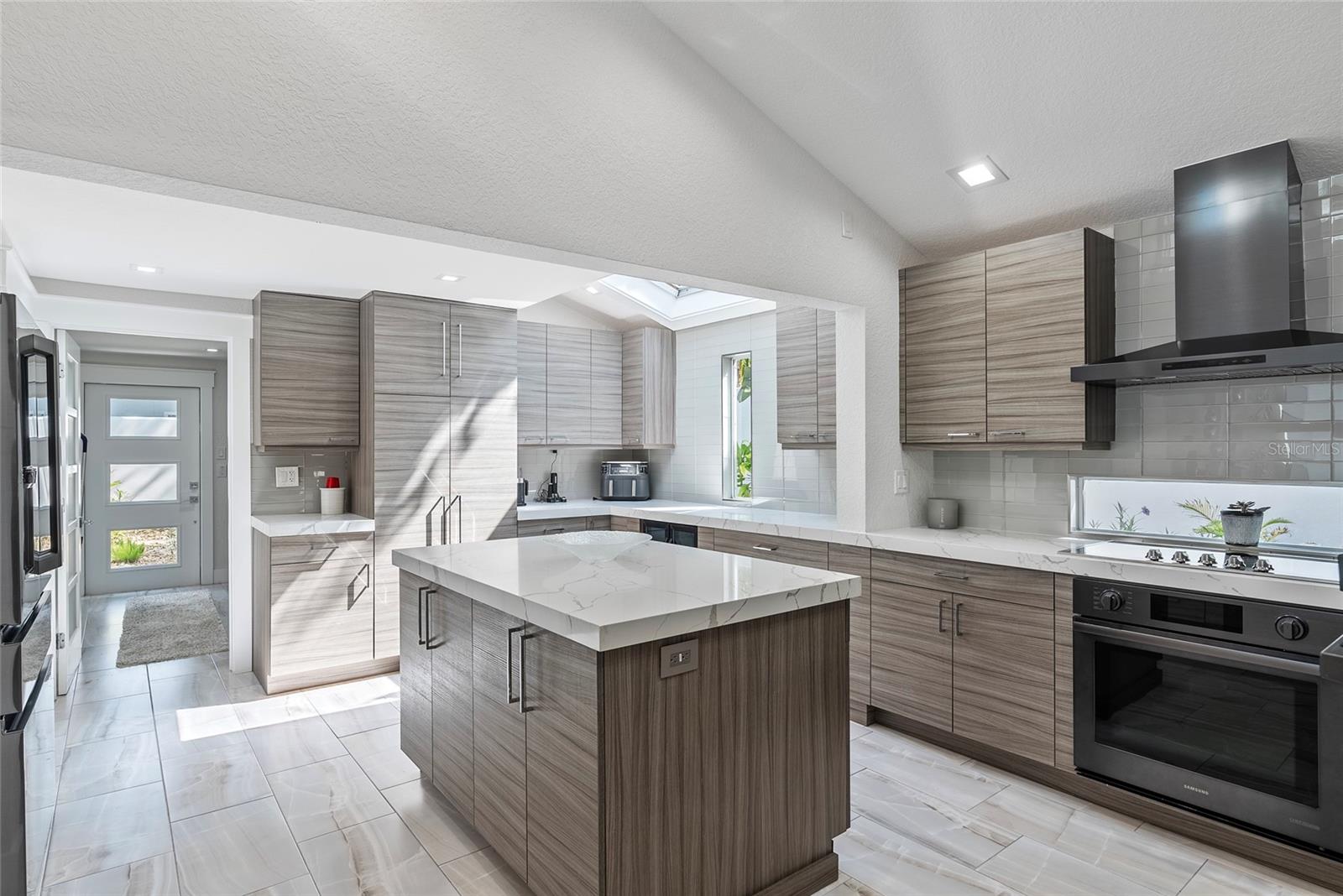 Modern kitchen with a large stone island, gray cabinets, and a skylight.