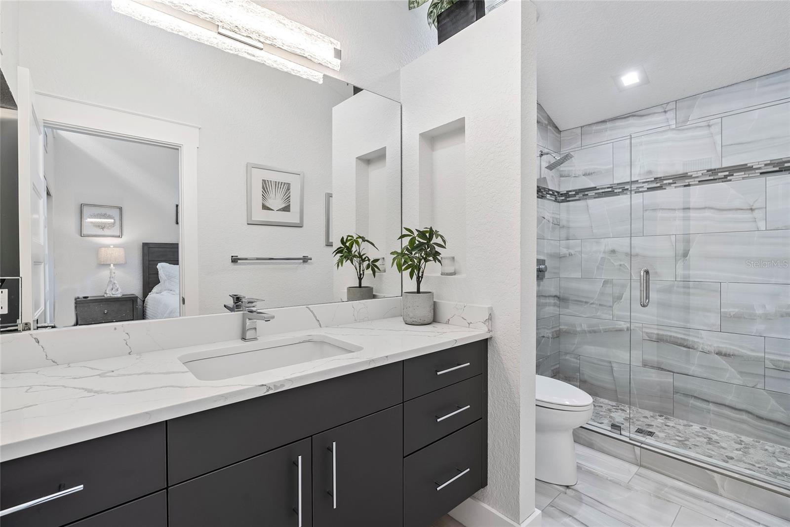 Bathroom with a dark gray vanity and glass shower tiled in gray marble-look panels.
