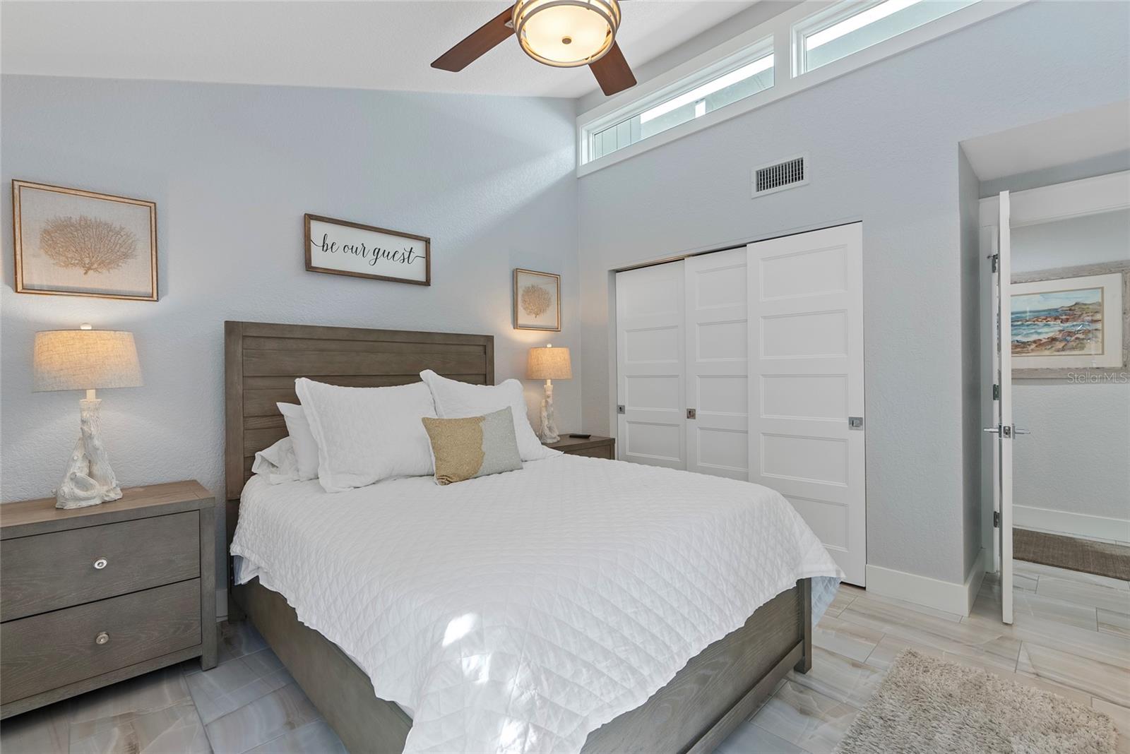 Guest bedroom with a white quilted bed, gray wood furniture, and high clerestory windows.