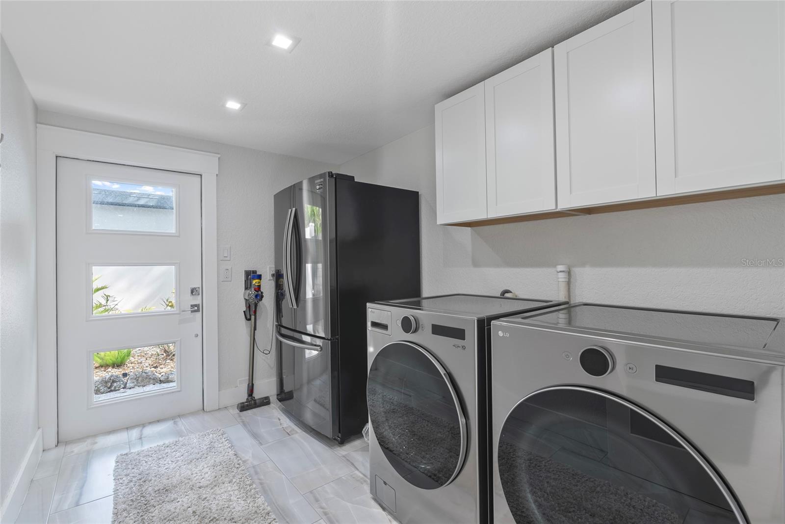Laundry room with front-loading washer and dryer, stainless refrigerator, and white cabinets.