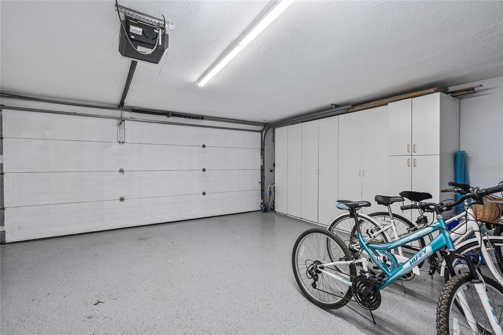 Garage with white storage cabinets, a closed overhead door, and several bicycles.