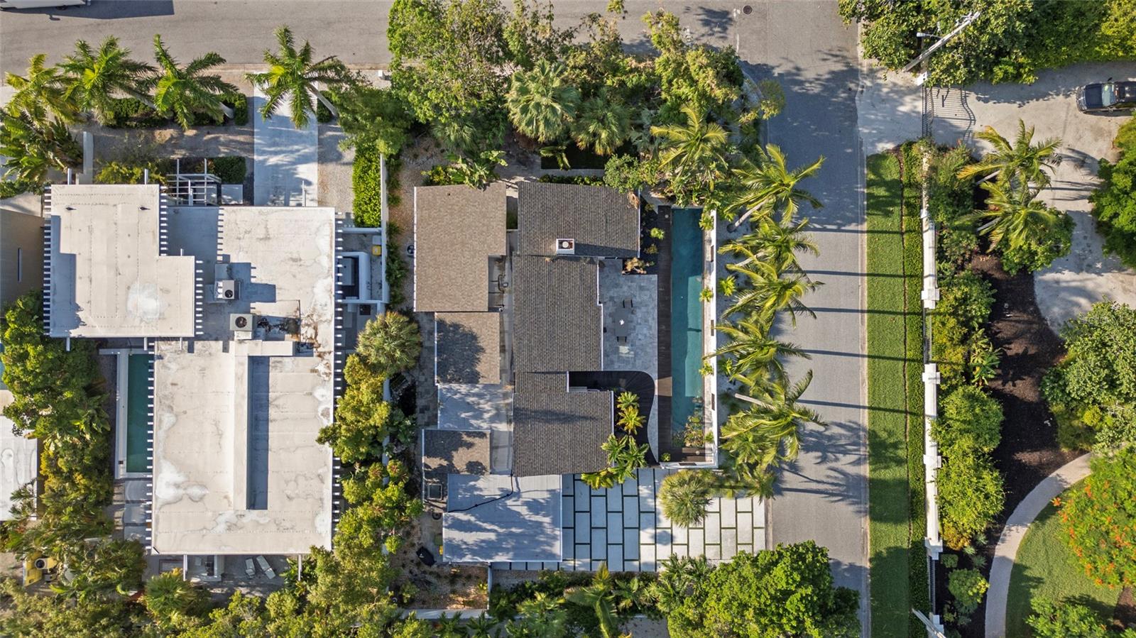 Aerial view of a residence with a long pool, paved patio, and palm-lined grounds.