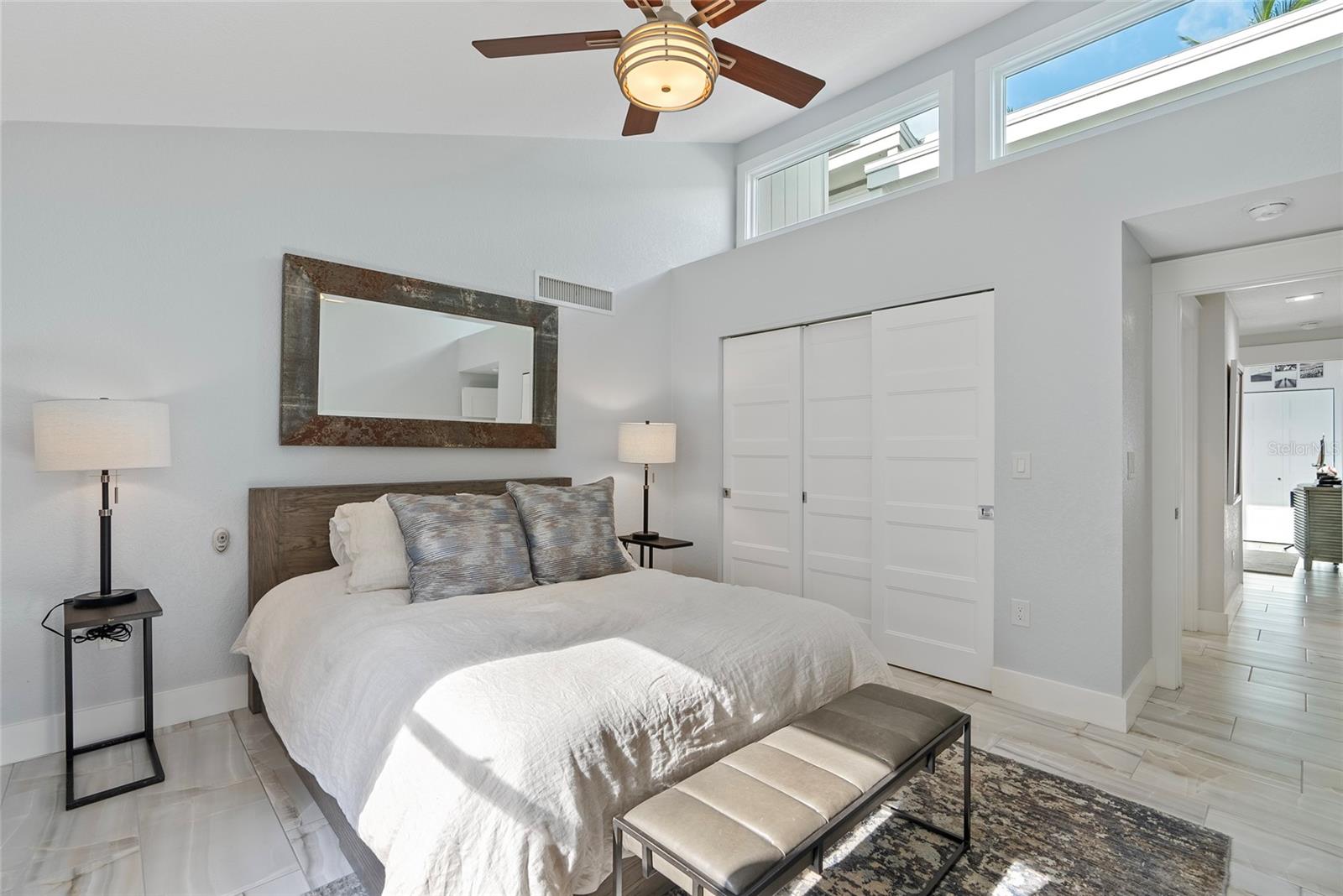 Furnished bedroom with a white bed, gray pillows, and high clerestory windows.