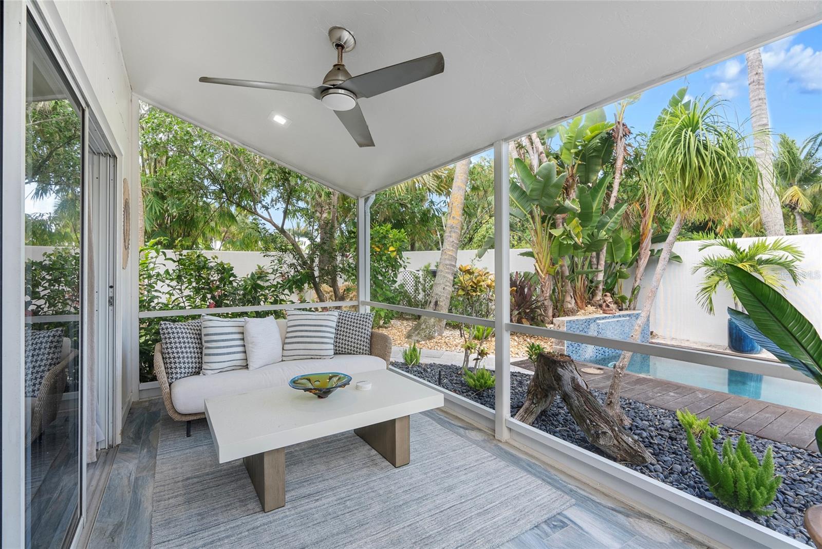 Screened lanai with cushioned seating and coffee table overlooking a tropical backyard pool.