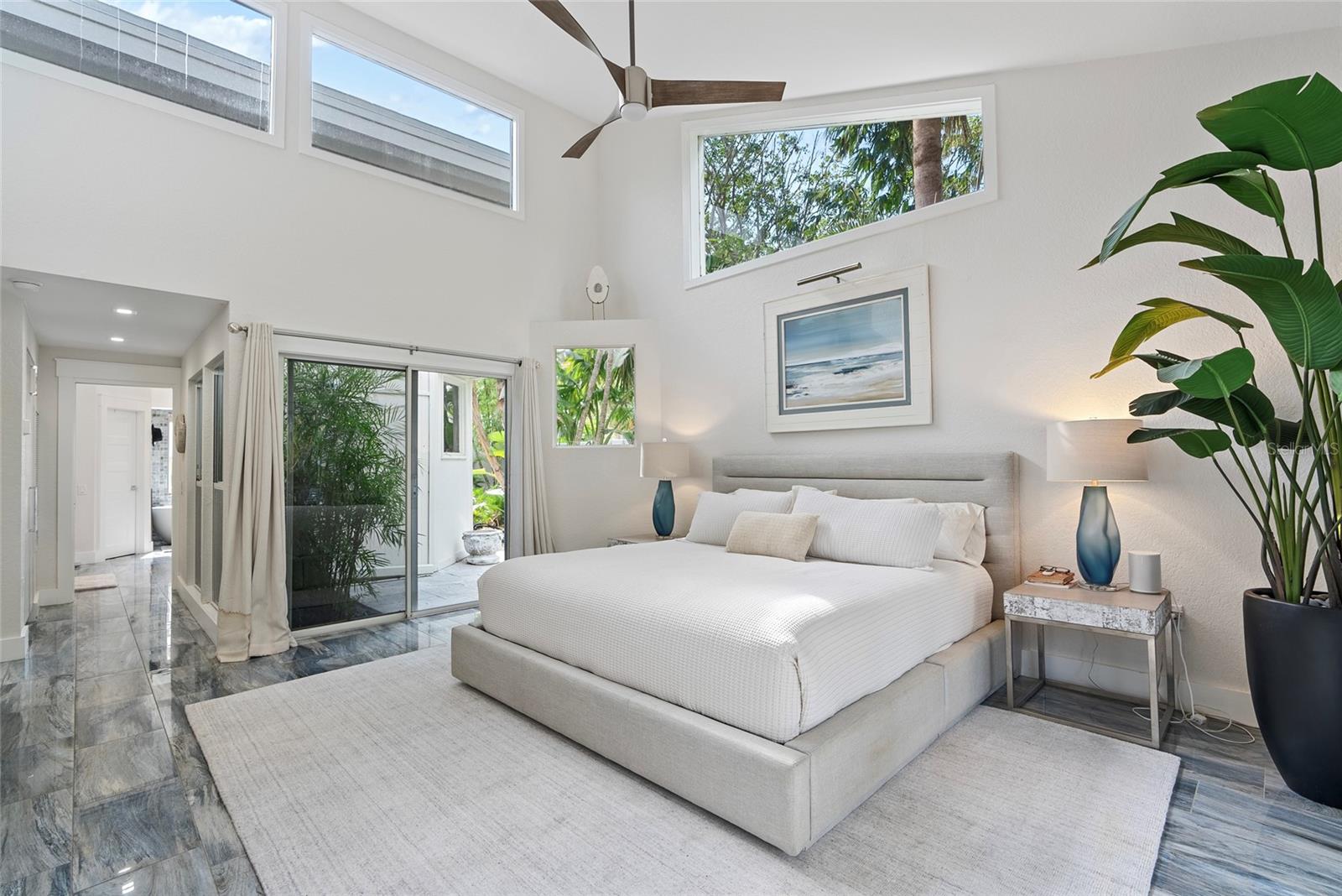 Primary bedroom with a vaulted ceiling, clerestory windows, and sliding glass doors opening toward tropical greenery.