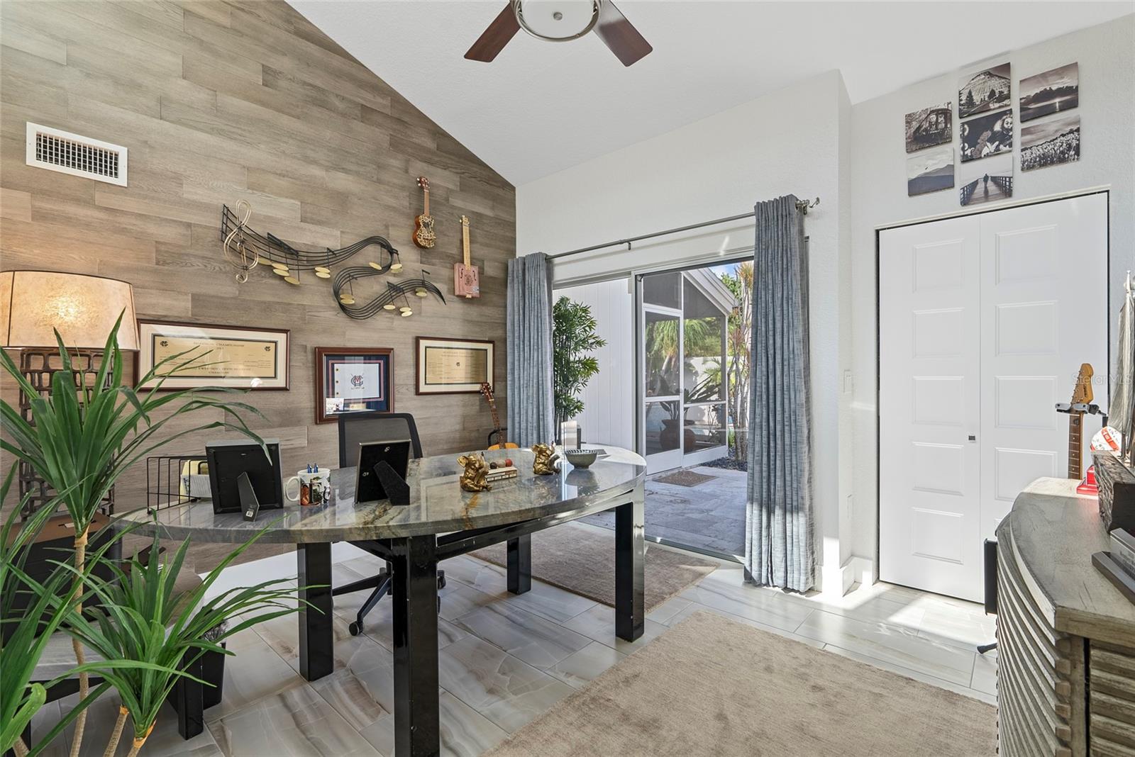 Home office with a curved desk, wood-look accent wall, and sliding glass doors to a patio.