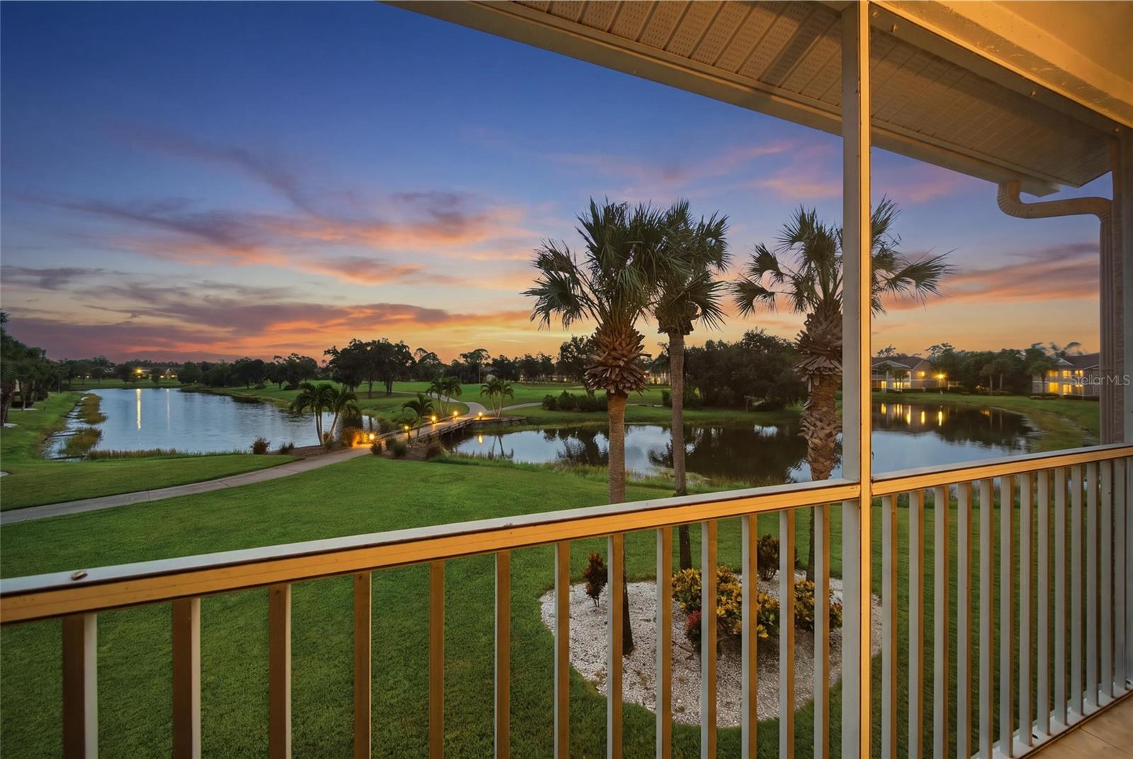 Covered balcony overlooking a golf course and ponds beneath a colorful sunset.