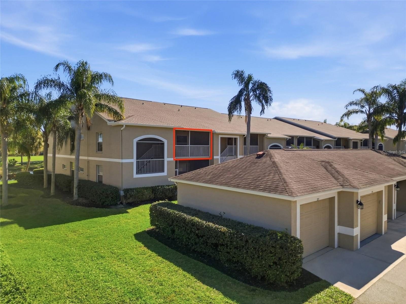 Condominium exterior with a red outline highlighting a second-floor balcony among palm trees and lawns.