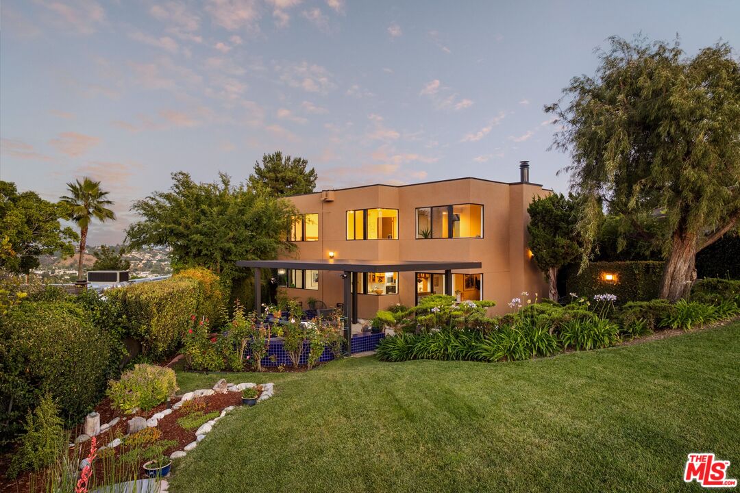 Modern two-story home at dusk, with warmly lit windows and landscaped gardens.