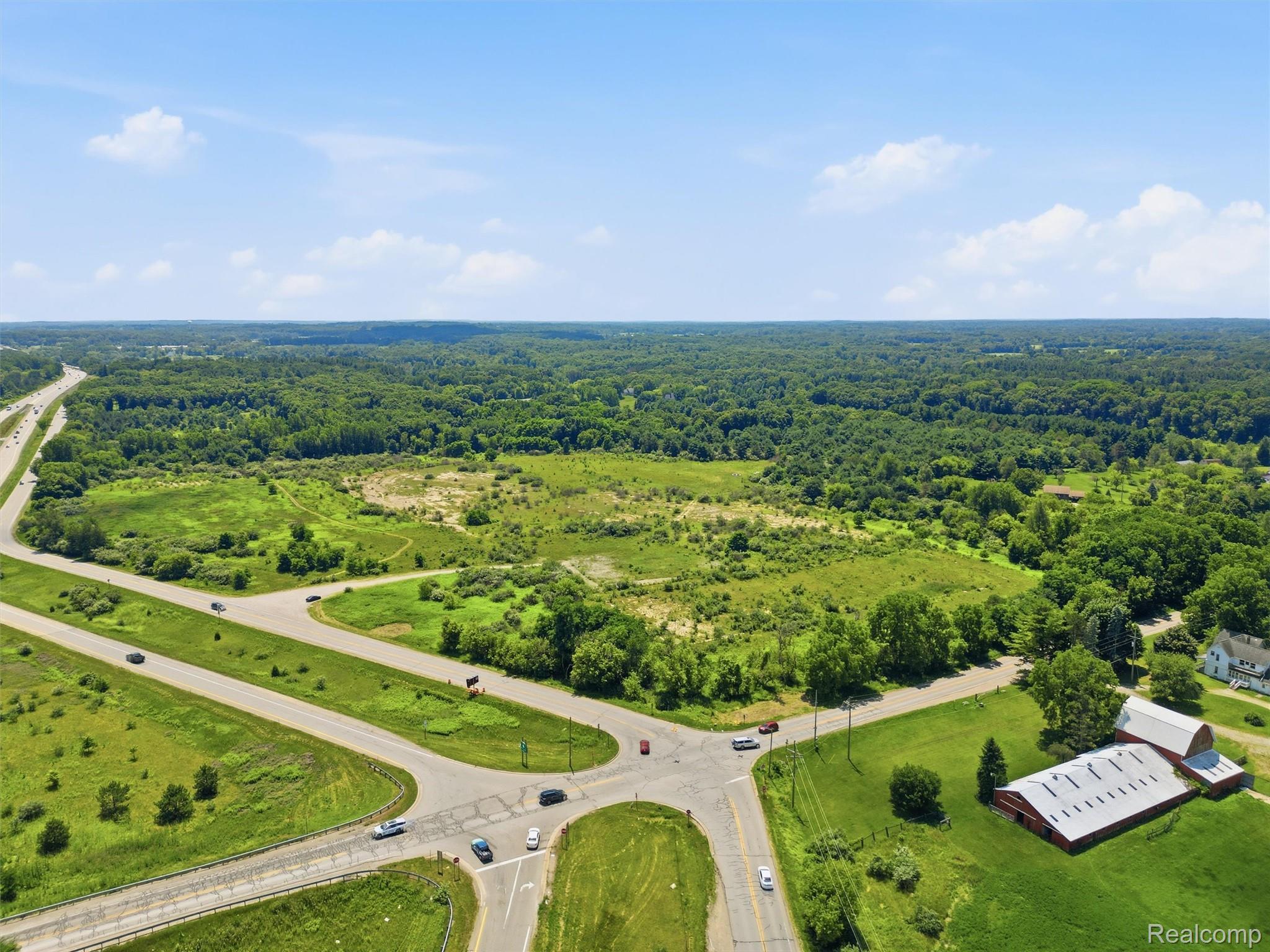 Aerial view of green, partly wooded land beside a road intersection and highway.