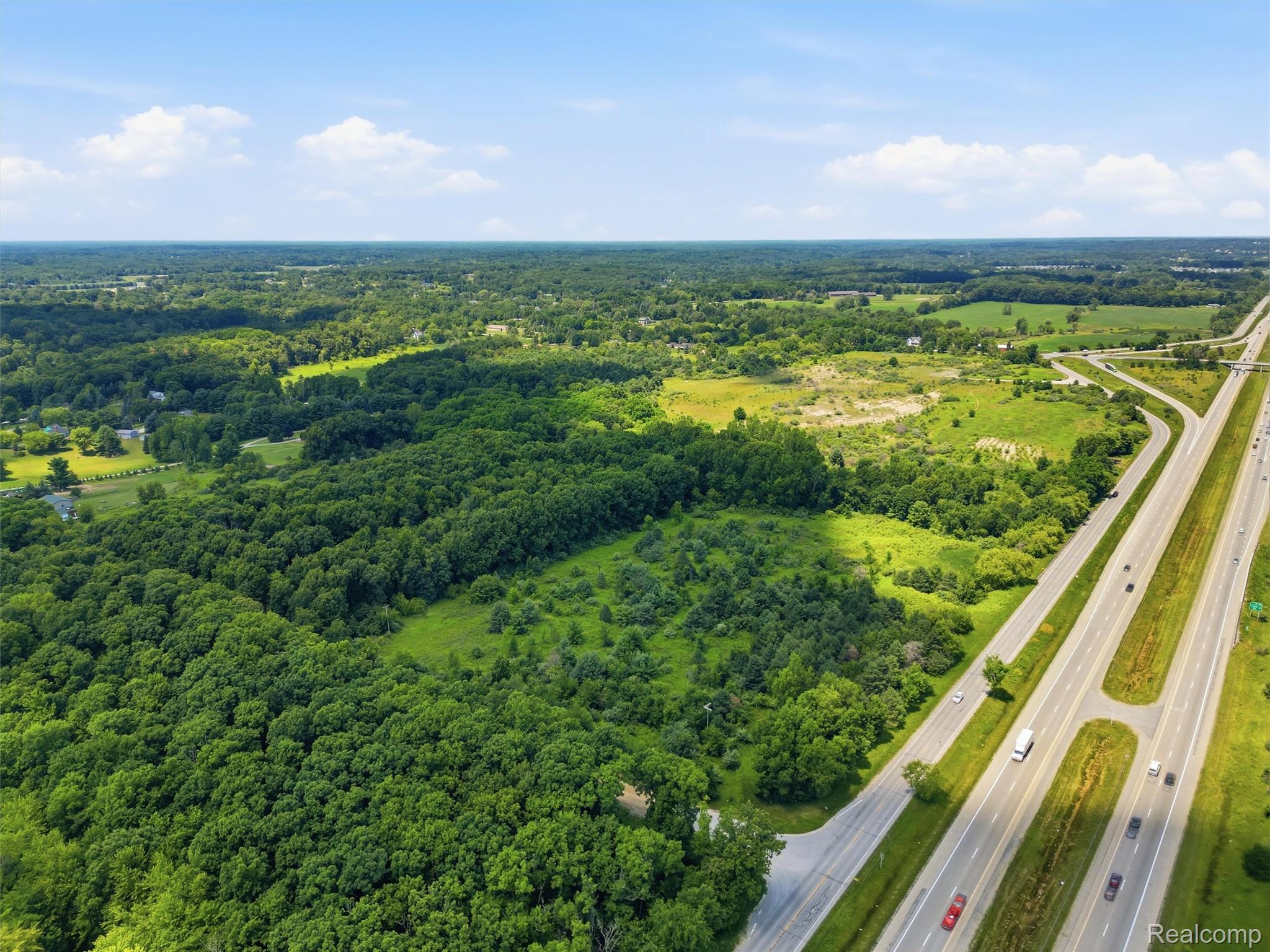Aerial view of wooded land and clearings beside a divided highway and interchange.