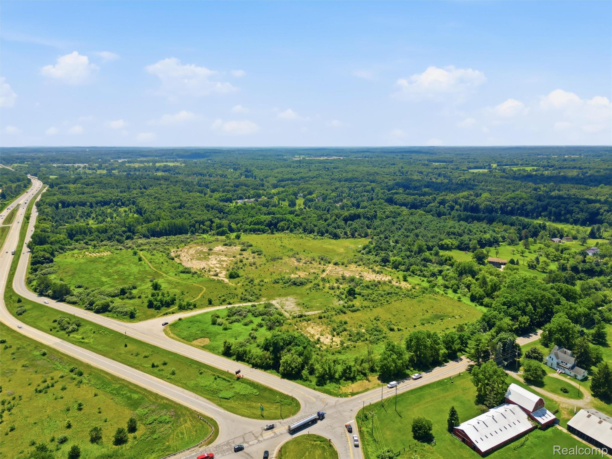 Aerial view of open grassy land bordered by woods, with roads and a highway nearby.