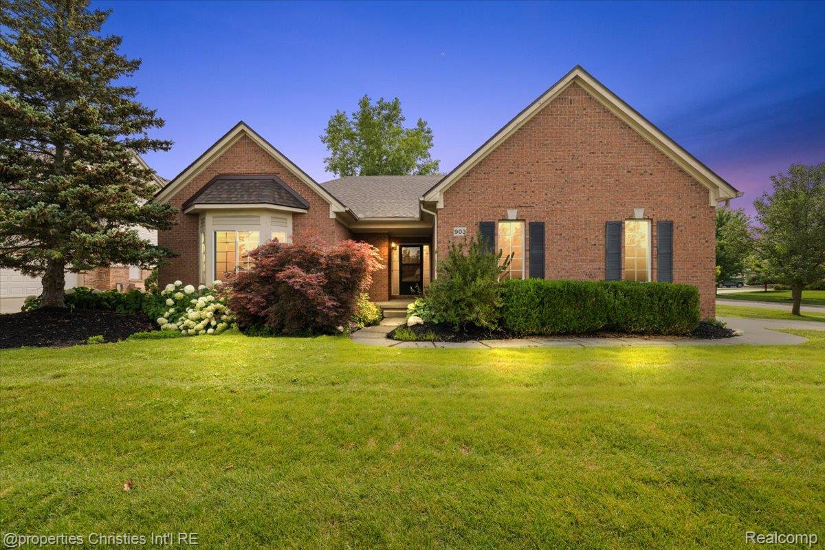 Red-brick home with prominent gables, landscaped front garden, and a broad lawn at dusk.