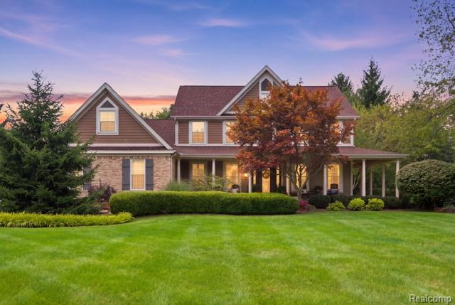Two-story home with stone and brown siding, a covered porch, and landscaped lawn at dusk.