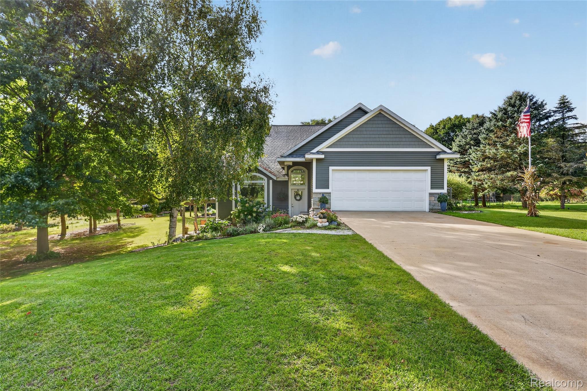 Gray house with white double garage, landscaped garden, mature trees, and broad green lawn.