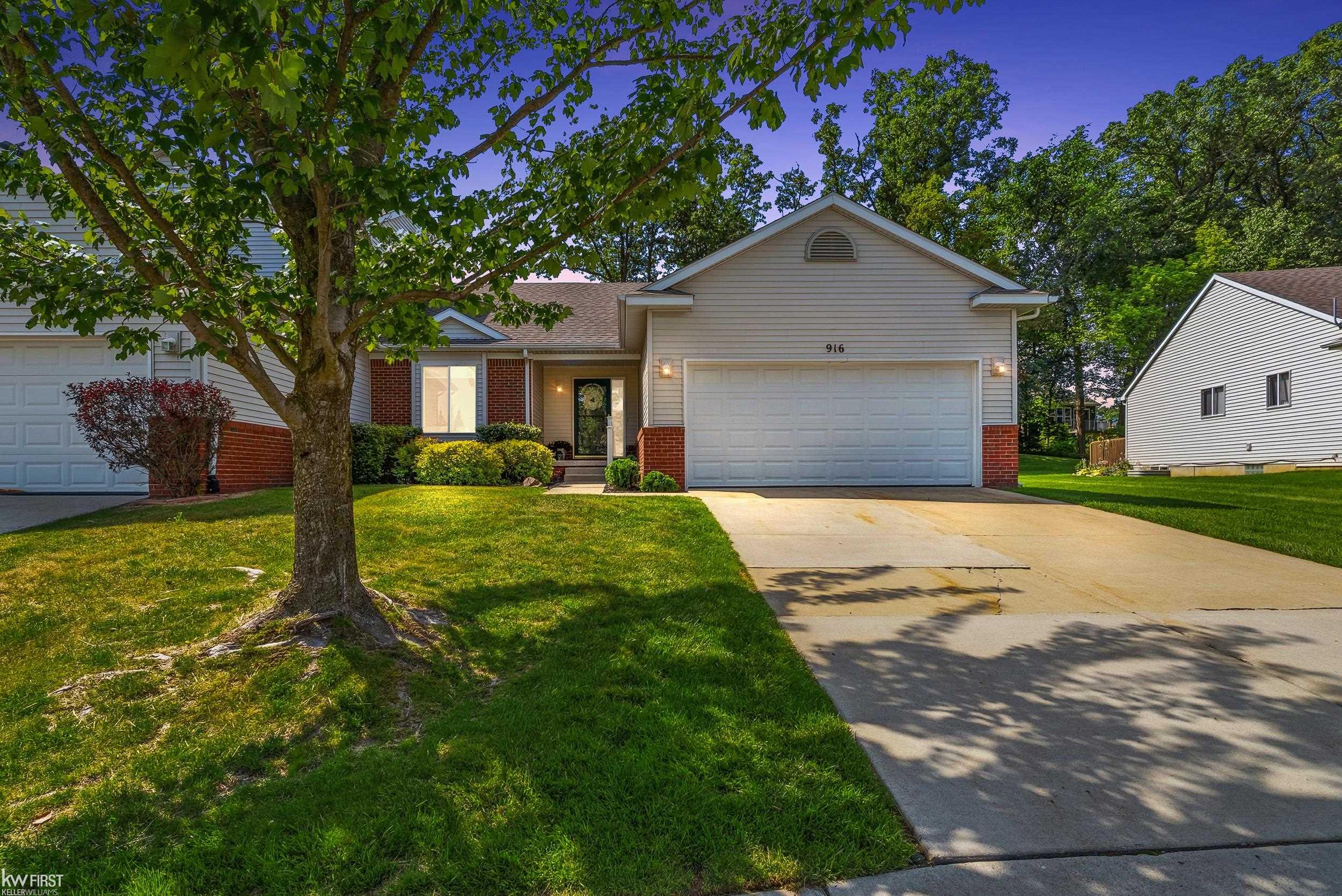 Suburban home with a two-car garage, brick accents, mature shade tree, and broad driveway.