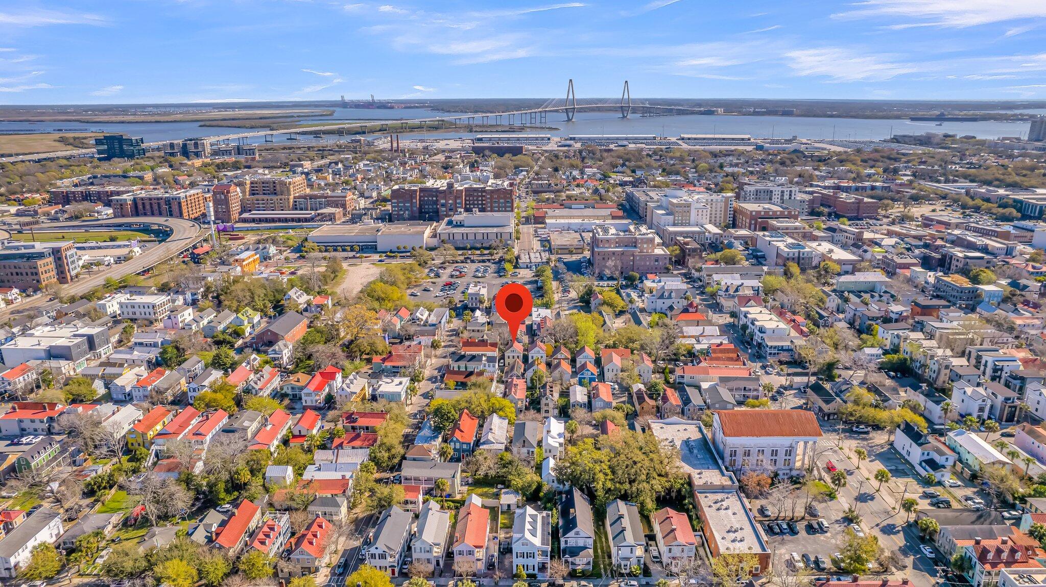 Aerial view of Charleston rooftops and the Cooper River, with the Ravenel Bridge on the horizon and a red location pin.