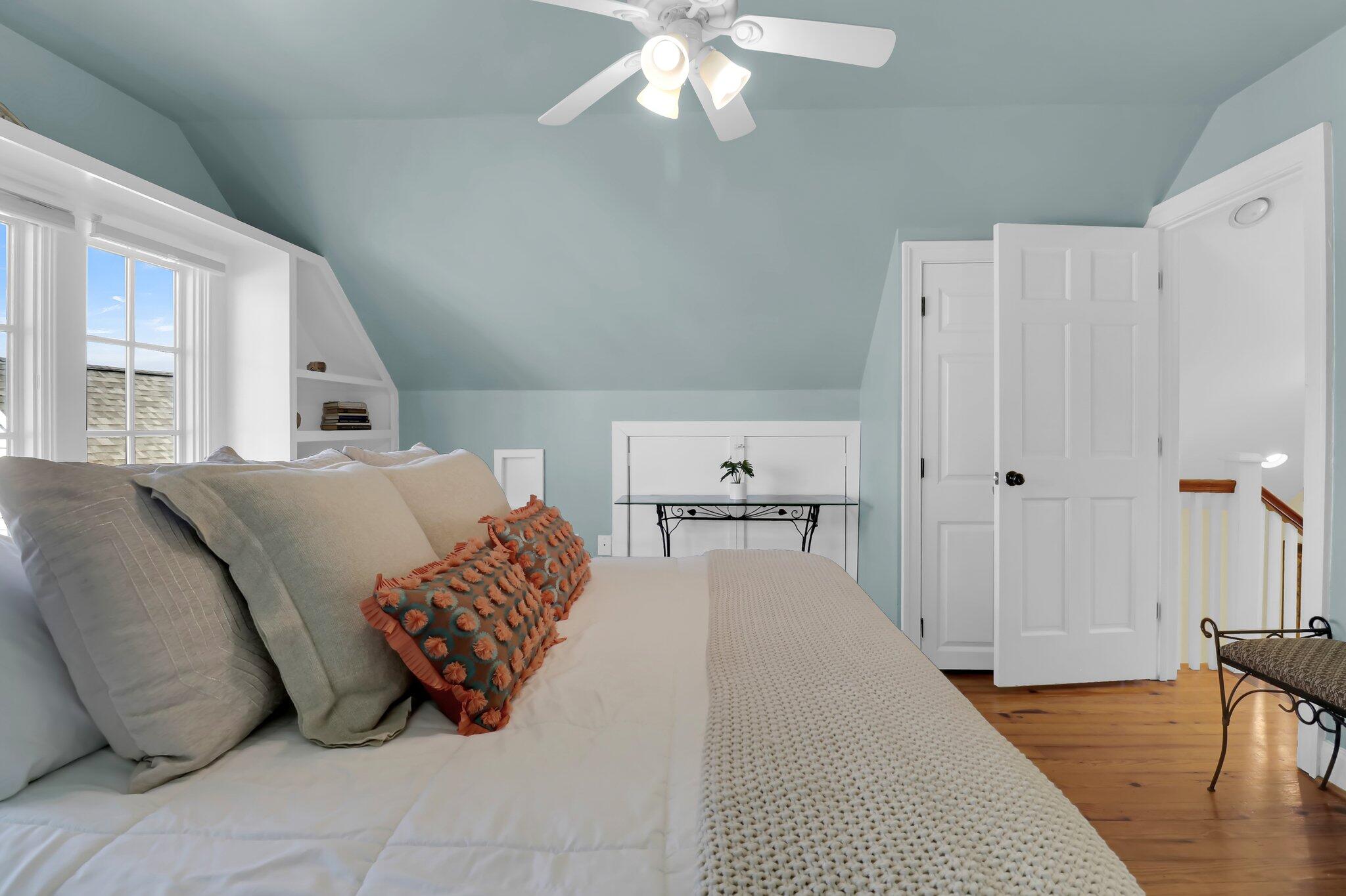 Attic bedroom with a sloped blue ceiling, layered pillows, built-in shelving, and an open door to the landing.