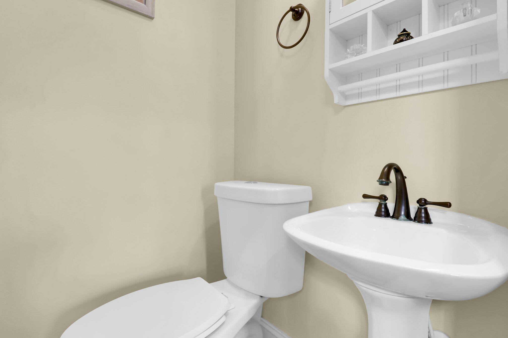 Bathroom with a pedestal sink, toilet, and white open-shelf wall cabinet.