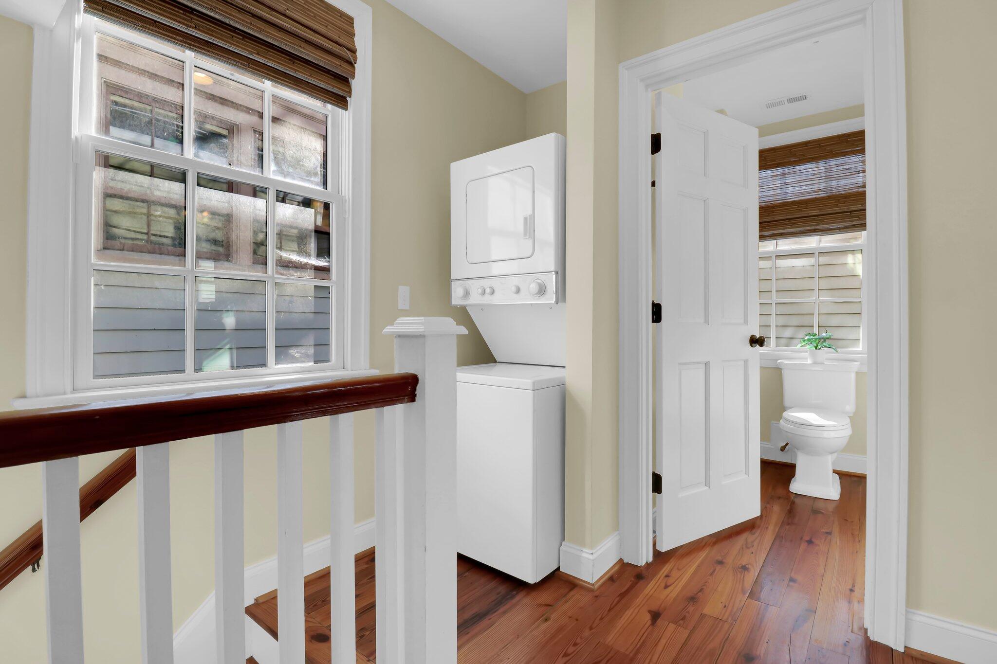 Hallway laundry nook beside a divided-light window, with an open doorway to a bathroom and hardwood floors.