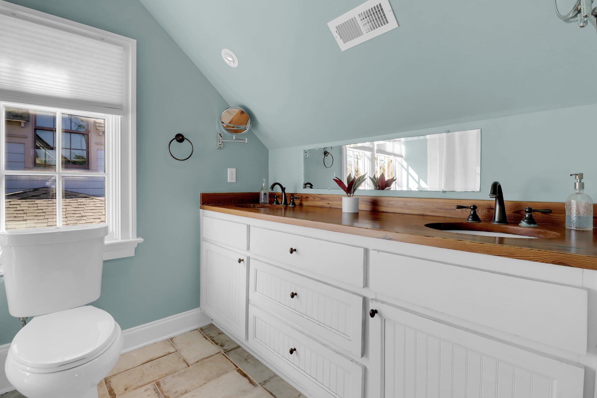 Bathroom with a double-sink vanity and warm wood countertop beneath a sloped ceiling.